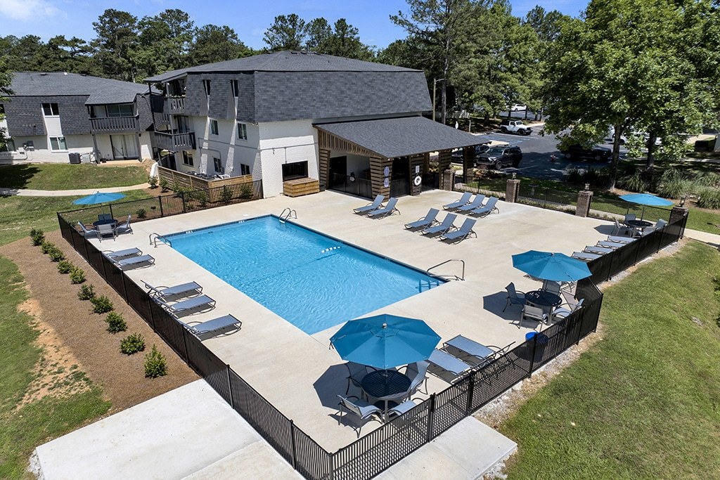 A large swimming pool surrounded by a black fence and blue umbrellas.